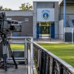 Leeg uitzendplatform langs het veld van KSK Heist met een vast clubembleem aan de stadioningang.