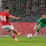 Een voetballer in rood neemt een strafschop voor een doelnet.
