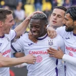Een groep Anderlecht-spelers viert samen een doelpunt in witte shirts met paarse accenten.