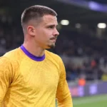Leander Dendoncker in een geel voetbalshirt in een stadionomgeving.