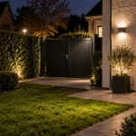 Verlichte tuin en gesloten toegangspoort bij een woning in de avond.