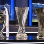 Drie Europese clubtrofeeën staan opgesteld in een televisiestudio.